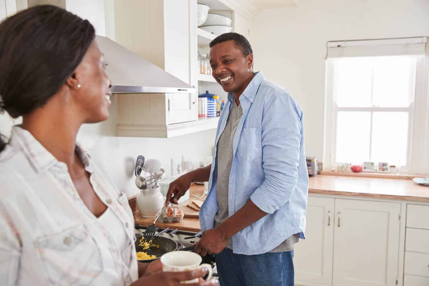 Mature Couple Chat In Kitchen As Husband Prepares Breakfast